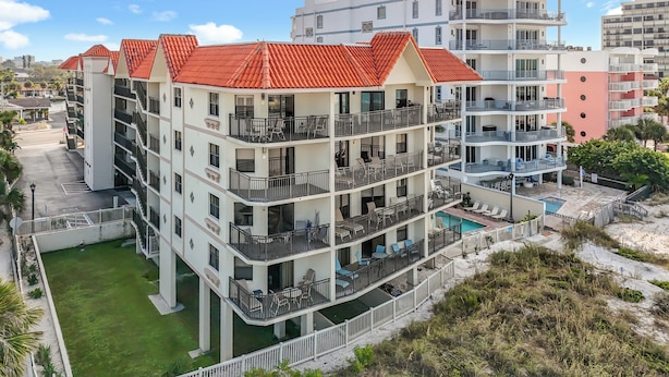 Un hotel de varios pisos con balcones, una piscina y un césped verde.
