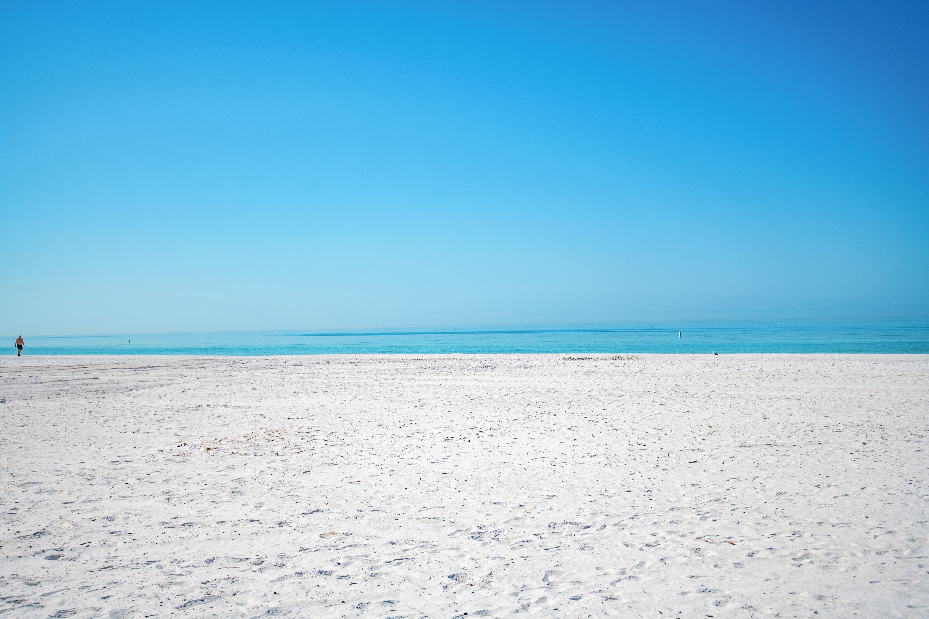 A wide, sandy beach with a clear blue sky and calm sea.