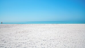 Una extensa playa de arena con cielo azul despejado y mar tranquilo.