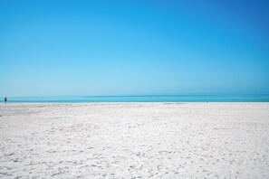 Una extensa playa de arena con cielo azul despejado y mar tranquilo.