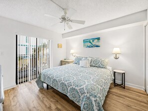 A bedroom with a bed, a ceiling fan, a nightstand, a lamp, and a painting on the wall.