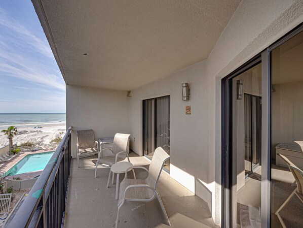 A balcony with a pool, chairs, and a view of the beach.