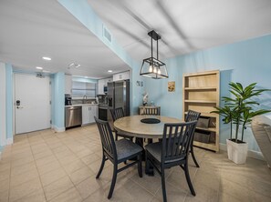A modern kitchen with stainless steel appliances, a dining area with a round table and chairs, and a light blue accent wall.