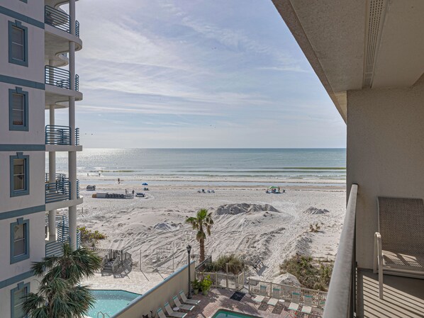 A beachfront hotel with a pool, beach chairs, and a view of the ocean.
