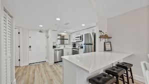 Een moderne keuken met witte kastjes, roestvrijstalen apparatuur en een bar met krukken.