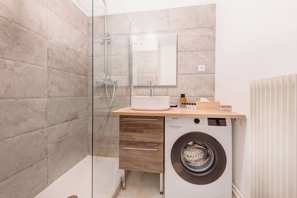 A modern bathroom with a glass shower enclosure, a built-in sink, and a front-loading washing machine.