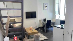 A modern living room with a sofa, a coffee table, and a TV. There is a dining area with a table and chairs. - Le Masséna d'Or: Quiet, Metro + Parc Tête D'or (Lyon)