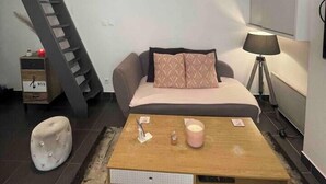 A compact room with a sofa bed, a small table with a lamp, a wall-mounted picture frame, and a staircase. - Le Masséna d'Or: Quiet, Metro + Parc Tête D'or (Lyon)