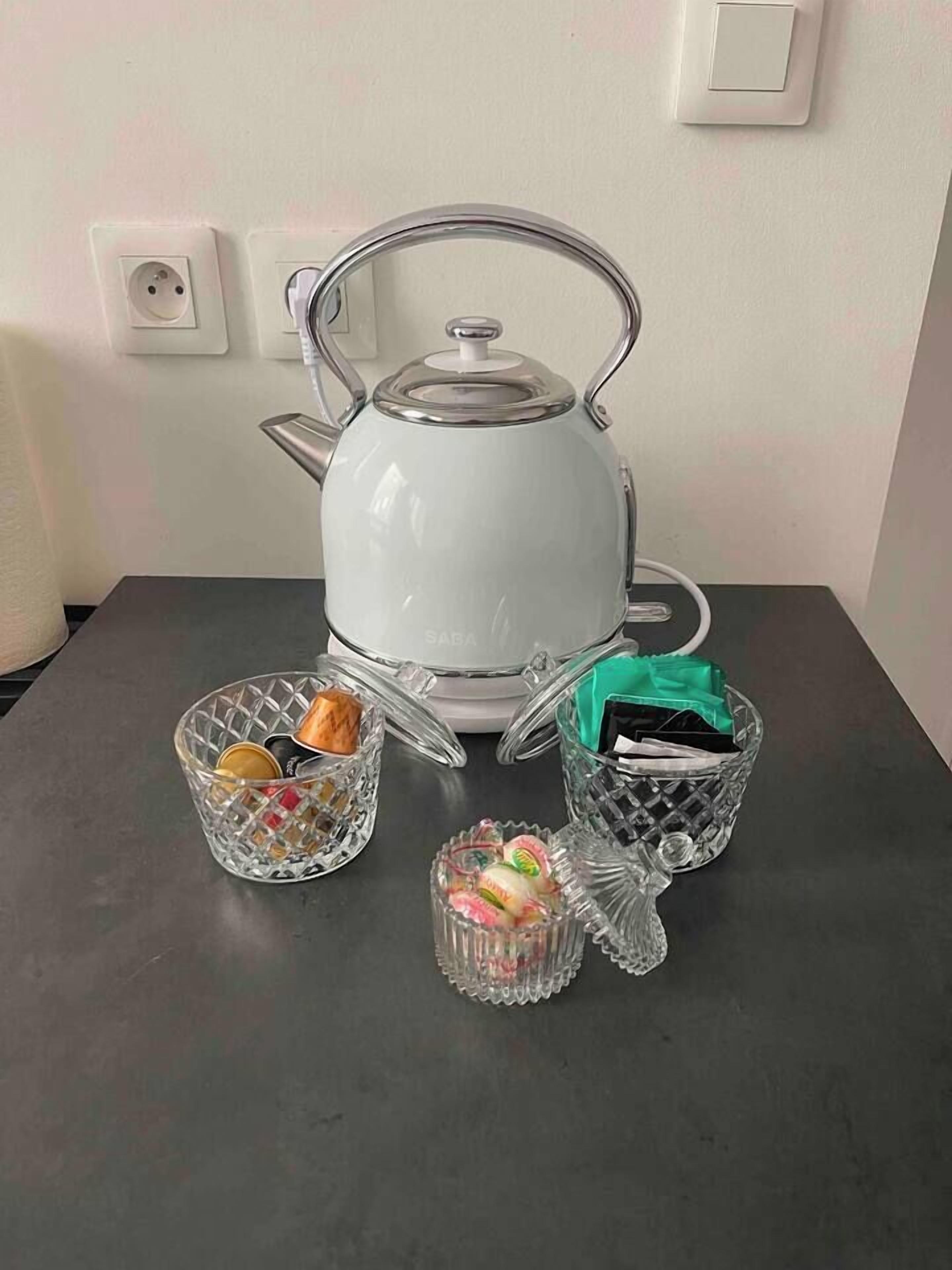 A white electric kettle on a table with two glass containers, one with snacks and the other with a green item.