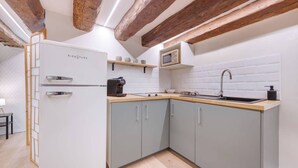 Une cuisine de taille réduite avec des meubles gris, un réfrigérateur blanc, un plan de travail en bois et des poutres apparentes en bois au plafond.