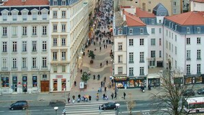 Une rue animée en milieu urbain, bordée de bâtiments des deux côtés, avec un passage piéton et quelques voitures sur la chaussée.