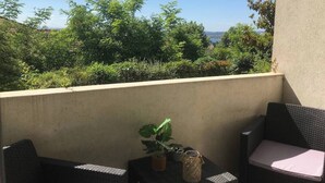 A balcony with wicker furniture, a potted plant, and a view of greenery and a distant landscape. - To complete (Lyon)