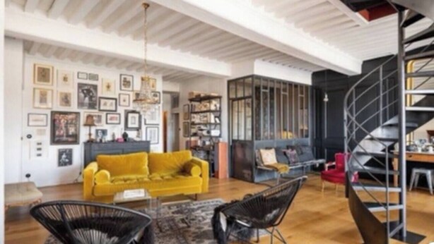 A spacious living area with a yellow sofa, black chairs, and a staircase.