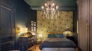 A bedroom with a large bed, a chandelier, a dresser, and a chair.