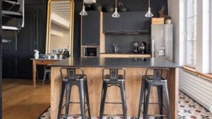 A modern kitchen with a central island, bar stools, pendant lighting, and a large mirror.