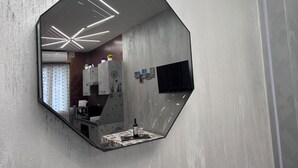 A hexagonal mirror with a geometric design, reflecting a modern kitchen with a built-in oven, a refrigerator, and a window with blinds.