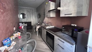 A modern kitchen with grey cabinets, a built-in oven, and a microwave. There is a dining area with a table and chairs.
