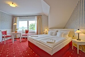 A hotel room with a large bed, two bedside tables, a small table with chairs, and a window with curtains. - Hotel Godewind (Mönchgut-Granitz)