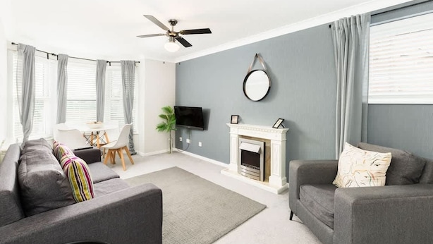 A modern living room with a grey sofa, a white fireplace, and a ceiling fan.