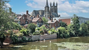 A historic building with a prominent tower, surrounded by lush greenery and a calm river.