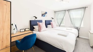 A hotel room with two beds, a desk, a chair, and a window with curtains.