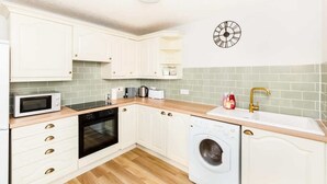 Une cuisine compacte avec des meubles blancs, un four à micro-ondes, un four traditionnel, un lave-linge et un évier doté d’un robinet doré.
