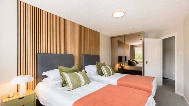Une chambre d’hôtel avec deux lits, un mur recouvert de lambris en bois, une table de chevet avec une lampe et un miroir.