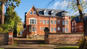 Un grand bâtiment en briques rouges, doté de nombreuses fenêtres et d’une tourelle d’angle imposante.