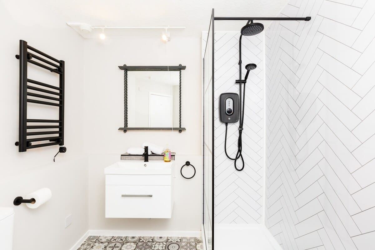 Ein modernes Badezimmer mit einem weißen Waschbecken, einem schwarzen Handtuchhalter, einem Spiegel und einer Dusche mit Duschbrause.