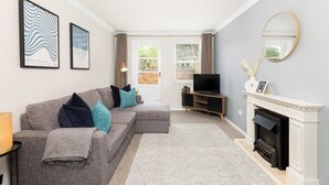 A modern living room with a grey sectional sofa, a fireplace, and framed artwork on the walls. - Modern | 2 Bed | Chestnut Court Leamington Spa (Royal Leamington Spa)