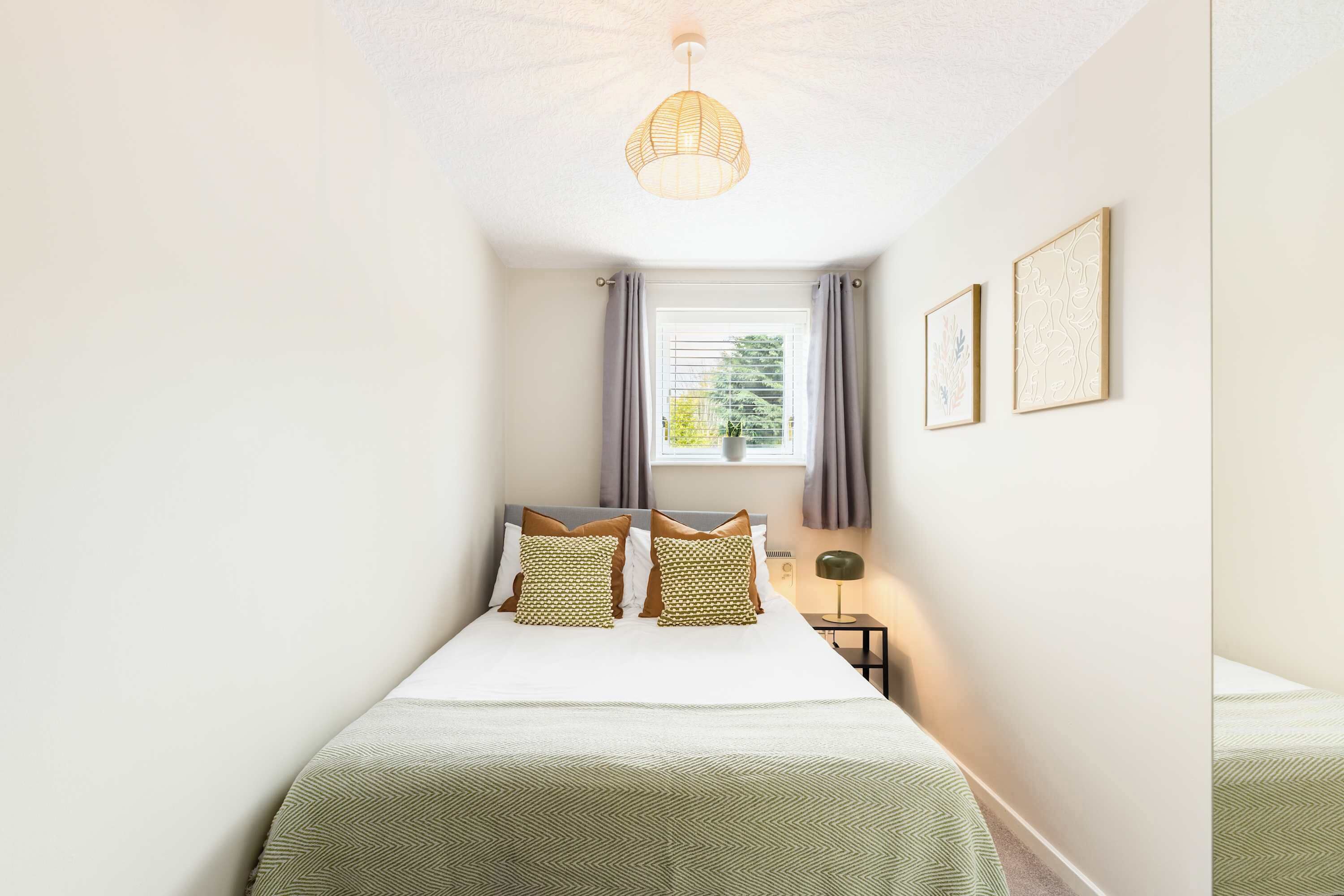 Une chambre à coucher bien rangée, avec un lit, une lampe de chevet et une fenêtre avec des rideaux.