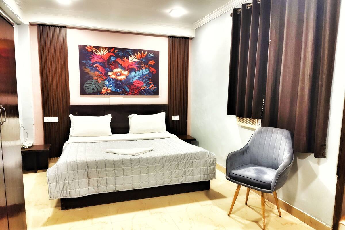 Una habitación de hotel con cama, una silla, un cuadro y una cortina.