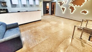 A hotel reception area with a reception desk, a blue sofa, a world map mural, and a tiled floor. - Hotel the terminal (New Delhi)