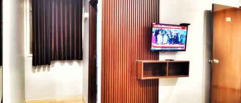 A room with a television mounted on the wall, a wooden door, and a patterned doormat on the floor.