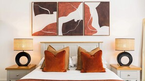 Une chambre d’hôtel avec un grand lit, deux tables de chevet avec des lampes et trois œuvres d’art abstraites accrochées au mur.