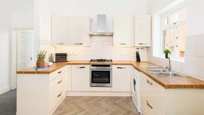 Une cuisine moderne avec des armoires blanches, un plan de travail en bois, un four encastré, un lave-vaisselle et une fenêtre qui laisse entrer la lumière naturelle.