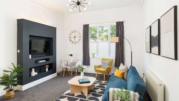Un salon moderne avec un téléviseur à écran plat, une table basse, un canapé, un fauteuil, une horloge et une fenêtre avec des rideaux.
