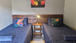 Habitación con dos camas, un cabecero de madera, una mesita con lámpara y un cuadro de un árbol en la pared.
