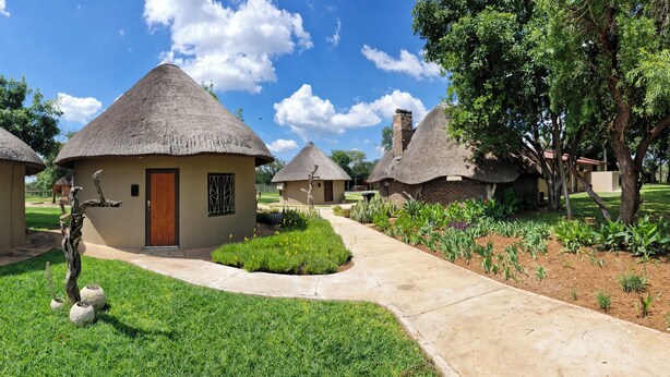 A row of thatched-roof cottages with a paved walkway and a well-maintained garden. - Buffelkraal Safaris (Mogalakwena)