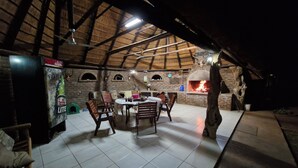 An outdoor dining area with a brick wall, wooden chairs, a table, and a pizza oven. - Buffelkraal Safaris (Mogalakwena)