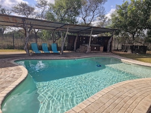 A swimming pool with a brick border, surrounded by a covered patio area with blue chairs. - Buffelkraal Safaris (Mogalakwena)