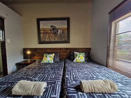 Habitación de hotel con dos camas, un cuadro de cebra enmarco, una lámpara y una ventana con persianas.