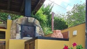 Un edificio amarillo con chimenea de piedra, puertas de madera y una maceta grande con flores rosa y blancas.