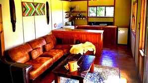 A cozy living room with a brown leather sofa, a wooden coffee table, and a patterned rug. - Enchanting Forest Cabin in Tsitsikamma (Stormsriver, Tsitsikamma)