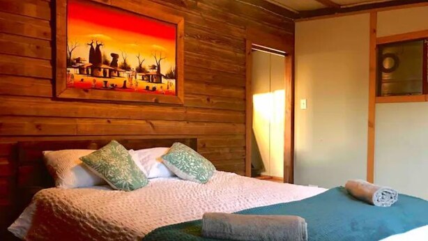 A wooden room with a bed, a painting, and a window. - Enchanting Forest Cabin in Tsitsikamma (Stormsriver, Tsitsikamma)