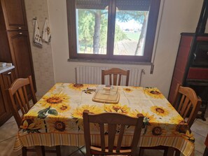 Un coin repas avec une table recouverte d’une nappe à motifs de tournesols, entourée de chaises en bois.