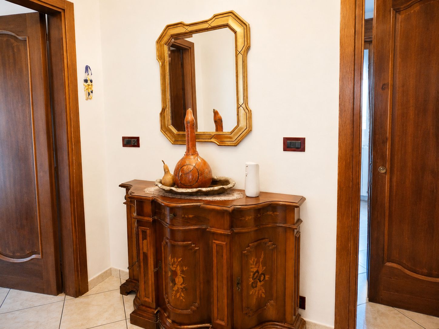A wooden cabinet with a mirror above it, a vase, and a small white object on top.