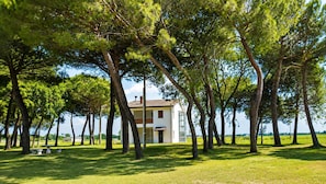 A two-story building surrounded by trees, with a grassy area in front.