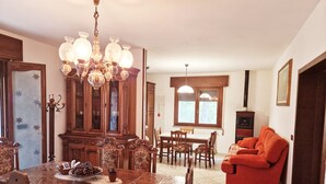 A dining area with a wooden table and chairs, a chandelier, and a red sofa in a room with tiled flooring and a window. - Cà Elena house located in the Po Delta park a few kilometers from Lido di Volano  (Emilia-Romagna)