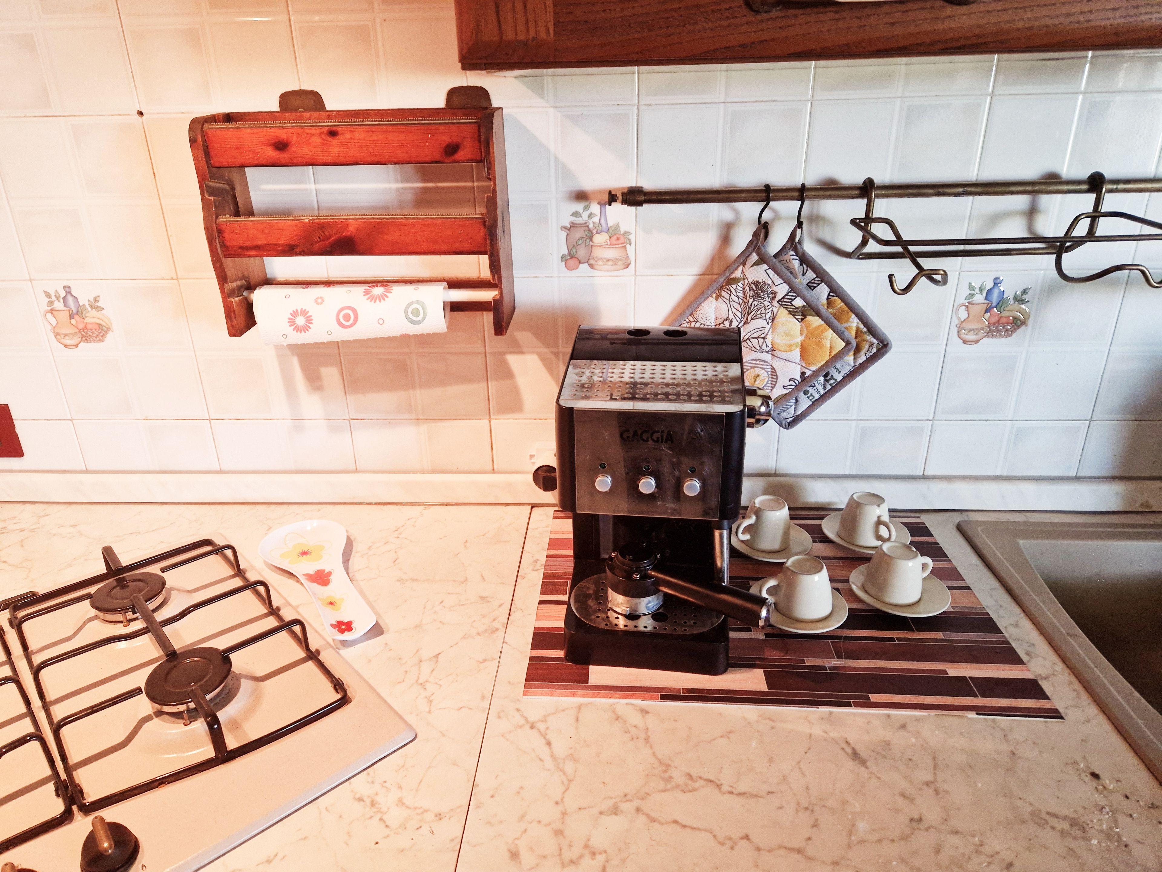 A kitchen with a gas stove, a coffee machine, and a hanging rack with pots.